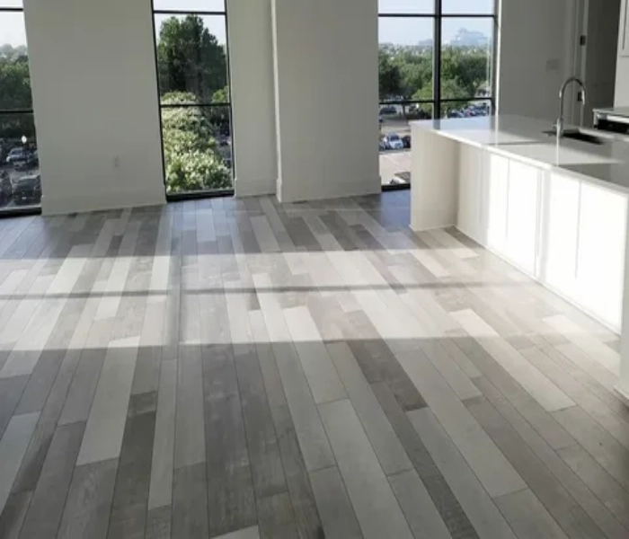 Modern open-plan kitchen and living space featuring grey and tan multi-toned LVP flooring planks that complement the bright white cabinetry.